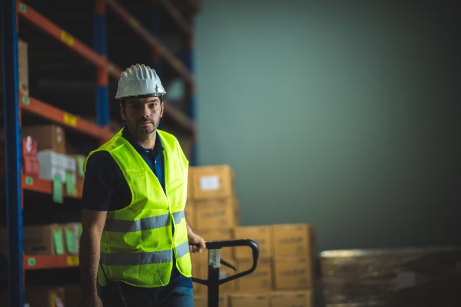 Male warehouse worker pulling a pallet truck in the storage warehouse